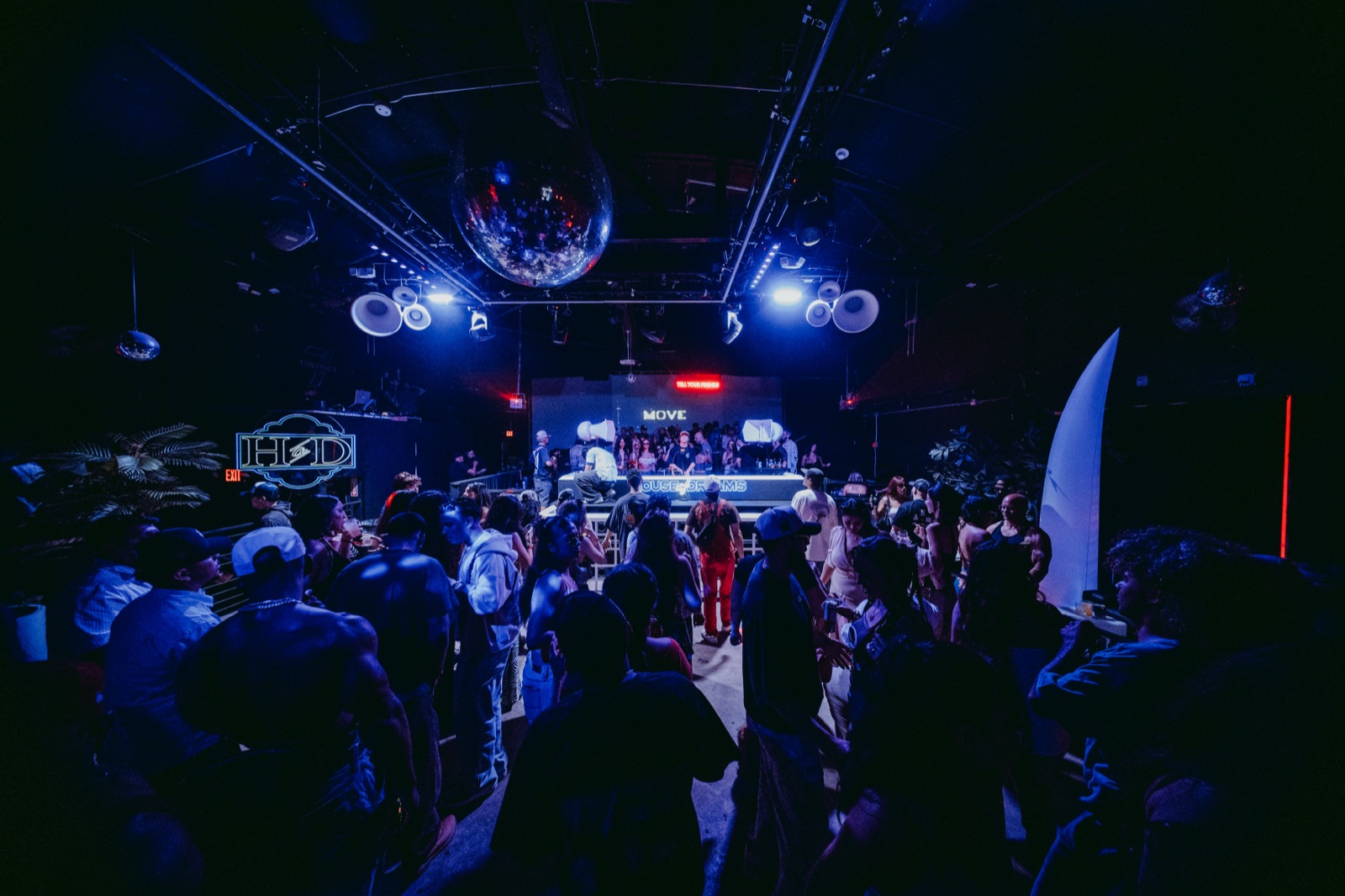 Packed dance floor lit blue beneath the disco ball with the District 7 neon sign